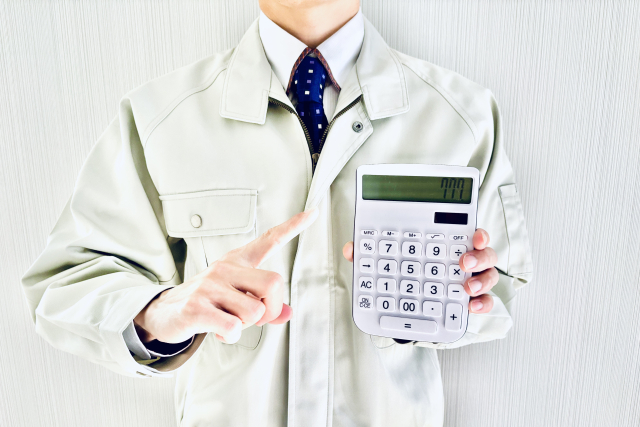 電卓を持って指さす作業服の男性