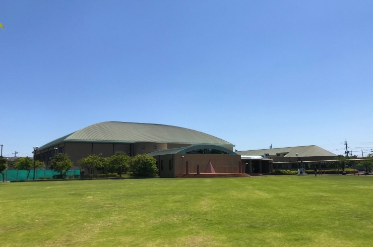 青空の下に広がる広い芝生と丸みのある大きな屋根の建物