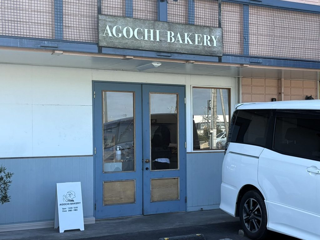 アゴチベーカリーの青い扉と木の看板がある店の正面