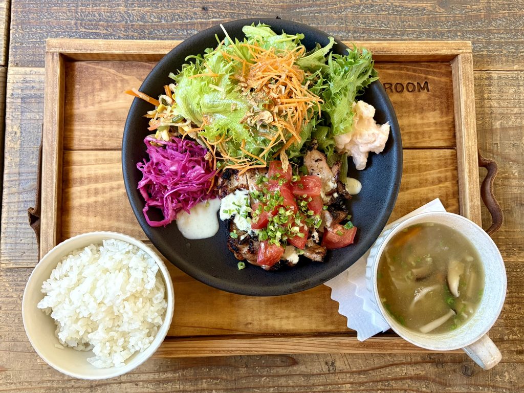 木製のトレーにのったトマトがのった鶏肉のグリルと生野菜のサラダと白米とスープの定食