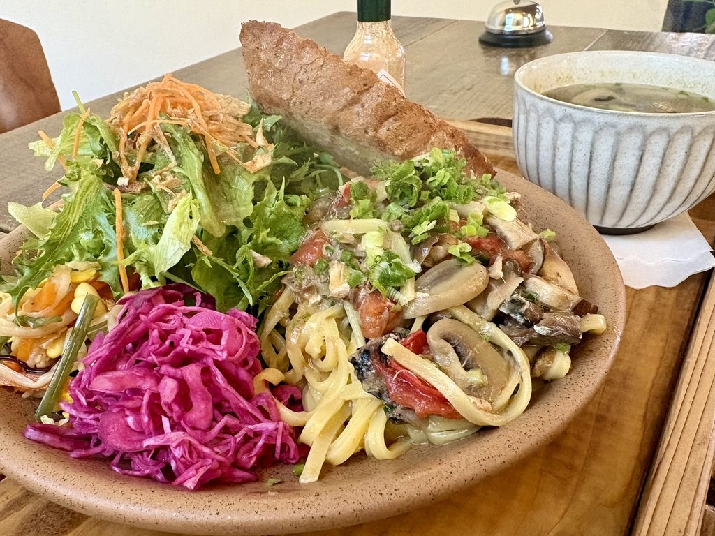 きのことトマトの平打ちパスタに生野菜サラダと紫キャベツ、厚切りパンを添えた一皿とカップに入ったスープ